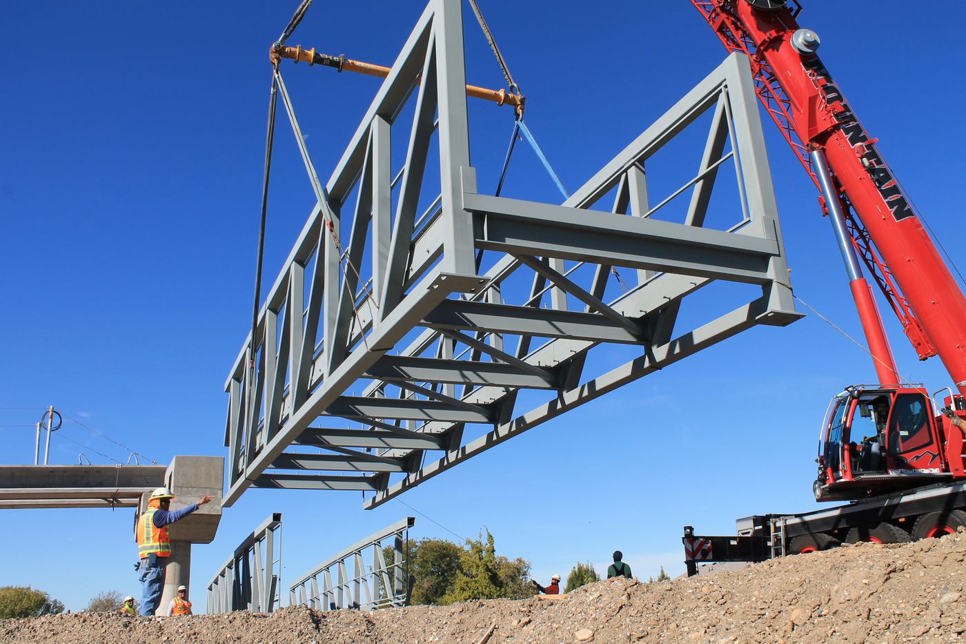 Crane setting a steel truss span into place at a bridge site