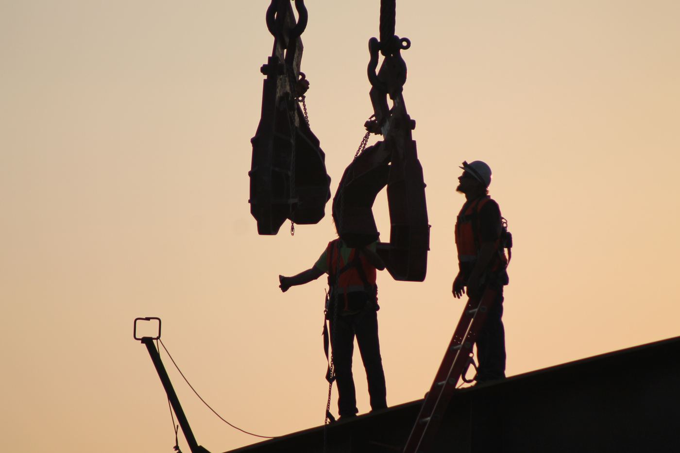 Ironworkers silhouetted against the sunset guiding a crane load