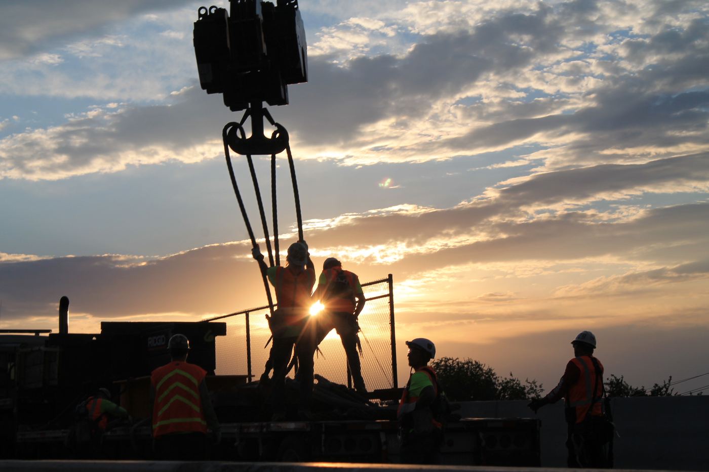 Crew silhouetted at sunrise preparing a crane lift
